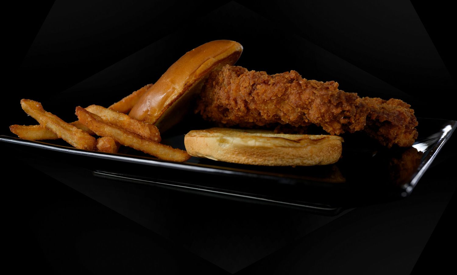 Crispy golden fried chicken tenders and French fries served on a black plate against dark background.