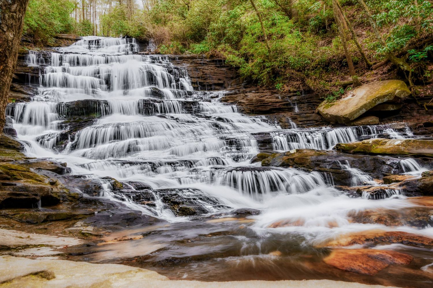Cascading waterfall flows over multiple tiers of rocky steps in a lush forest setting at Georgia's Minnehaha Falls.