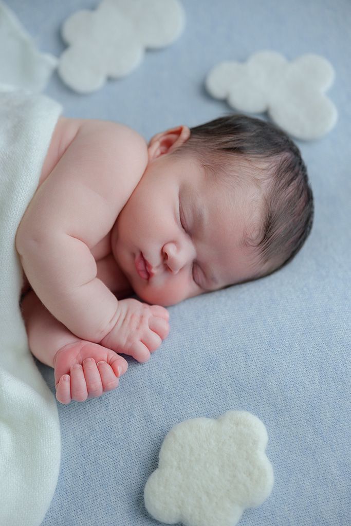 Peaceful newborn baby sleeping on a soft blue blanket surrounded by white felt cloud decorations.