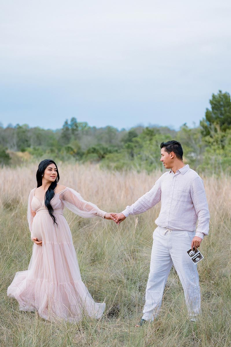 A couple dances together in a golden field wearing pink and white romantic outfits during a photo session.