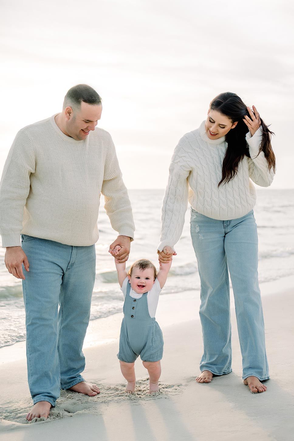 Three people walking barefoot together along the shoreline wearing matching blue and white outfits.