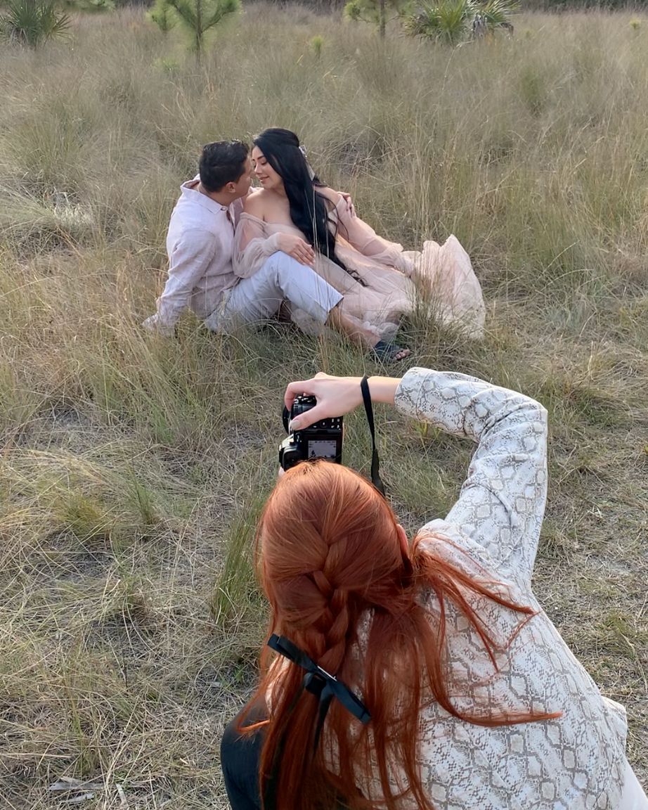 Couple embraces in an intimate moment while sitting on dry grassy terrain during golden hour.