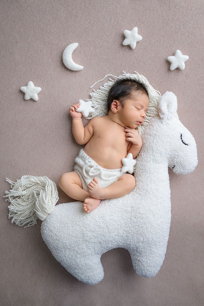 Newborn baby sleeping on a white unicorn plush toy surrounded by star and moon decorations.