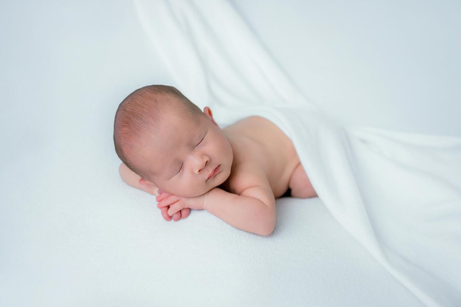 Peaceful newborn baby sleeping on a soft white blanket in a serene studio portrait.
