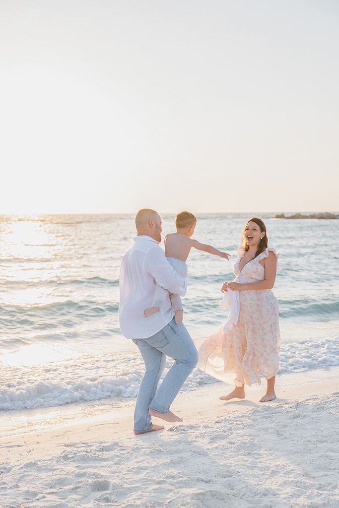 Happy family with child playing on beach at golden hour sunset.