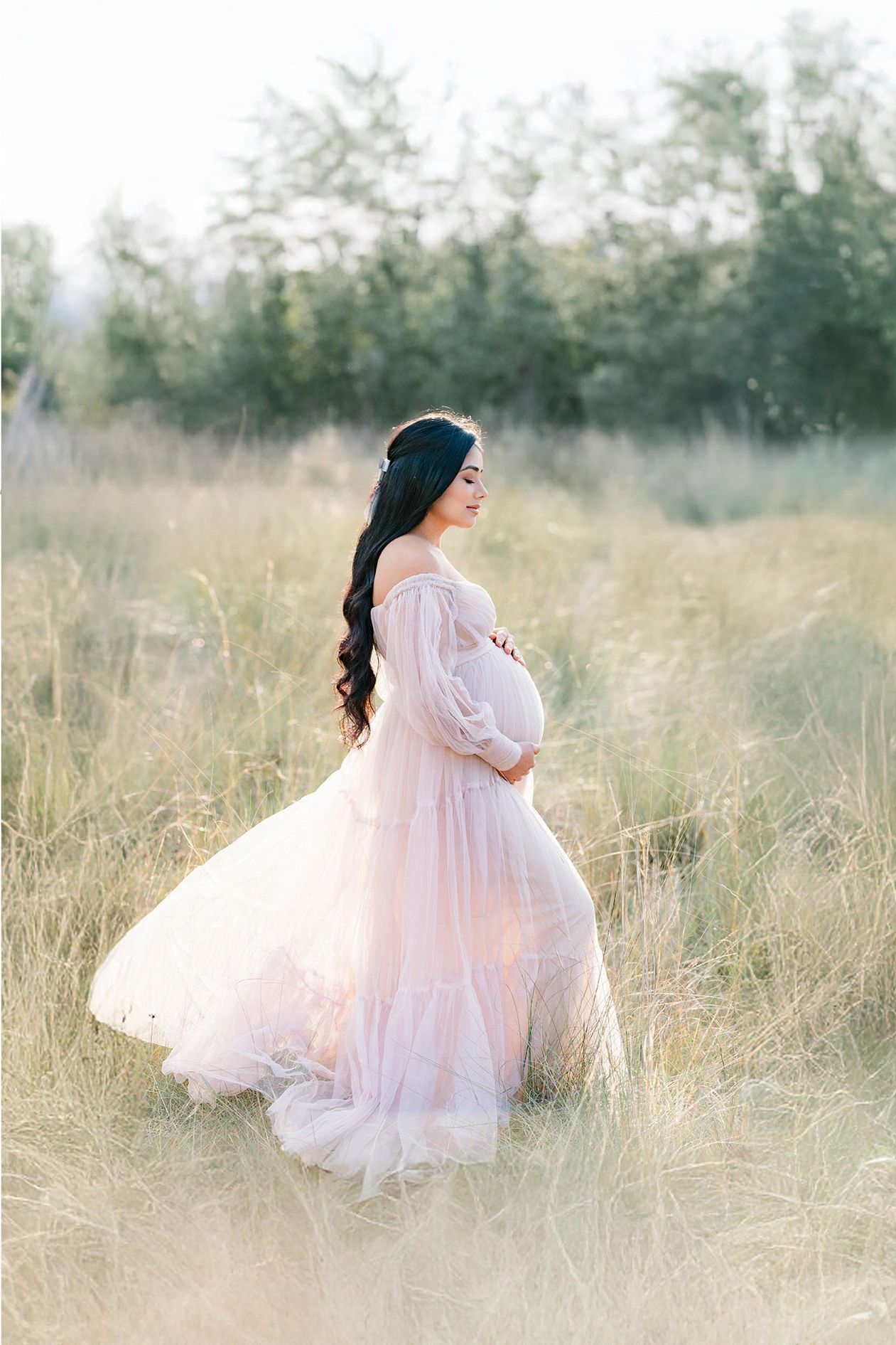 A figure in a flowing pink dress twirls gracefully through a sunlit meadow of tall grass in a dreamy outdoor setting.