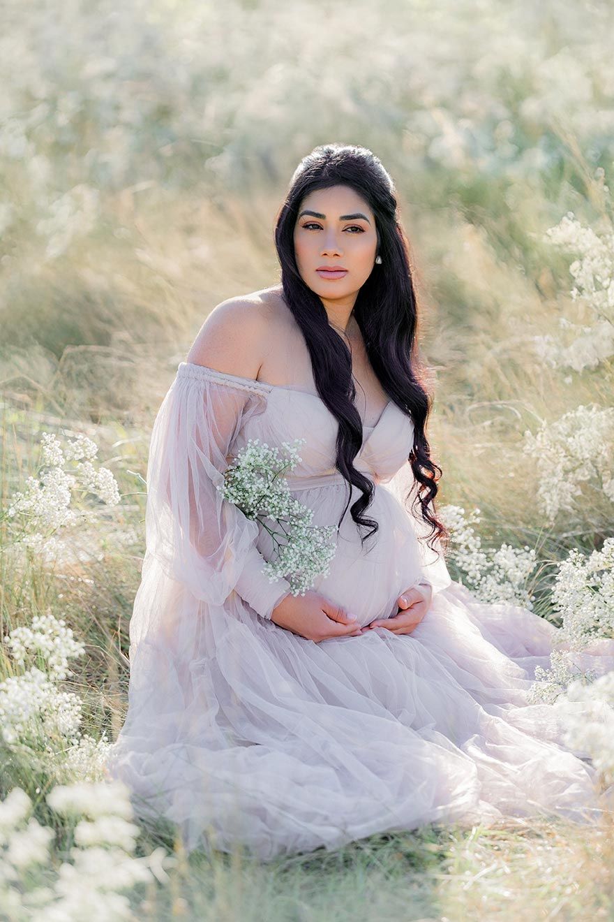 An ethereal photography session in a sunlit meadow features a flowing white dress among delicate wildflowers.