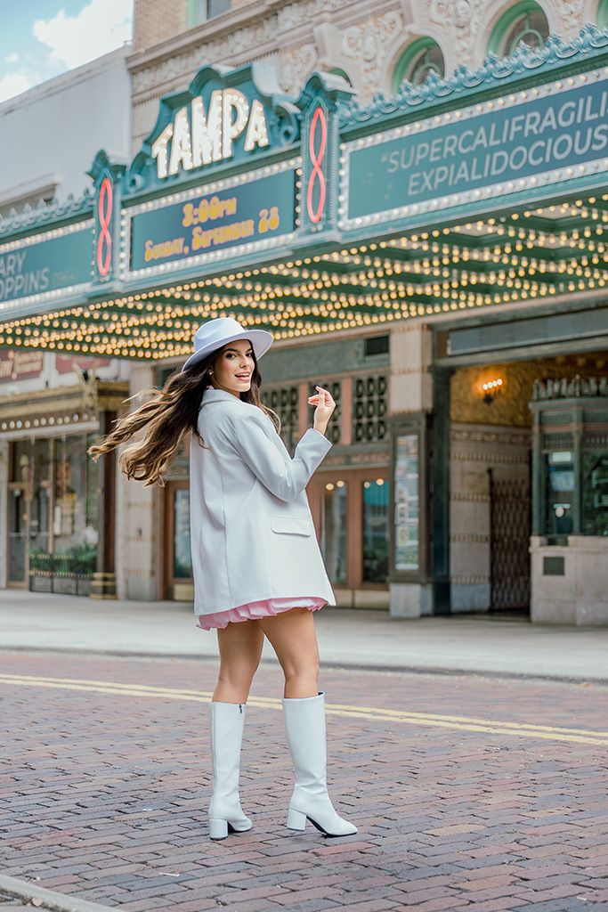 Woman in white blazer, hat, and boots posing in front of Tampa Theatre marquee showing Mary Poppins.