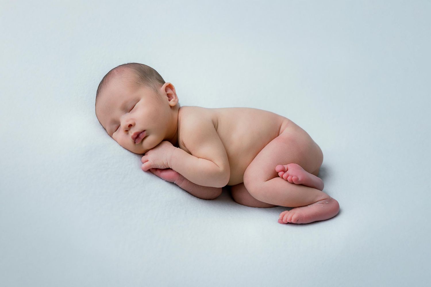 Peaceful sleeping newborn baby curled up on light blue background in studio setting.