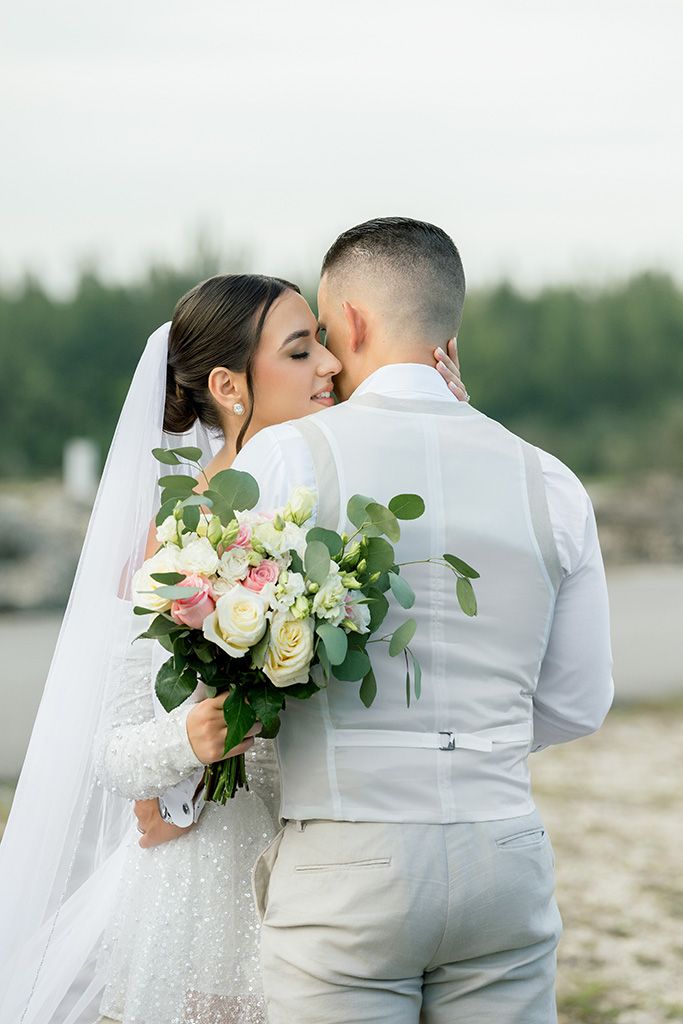 Bride and groom sharing a romantic moment outdoors, bride holding a bouquet of white and pink roses with eucalyptus.