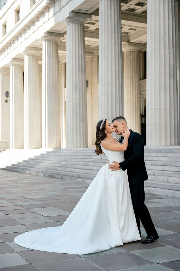 Wedding couple kissing in front of grand neoclassical building with tall stone columns.