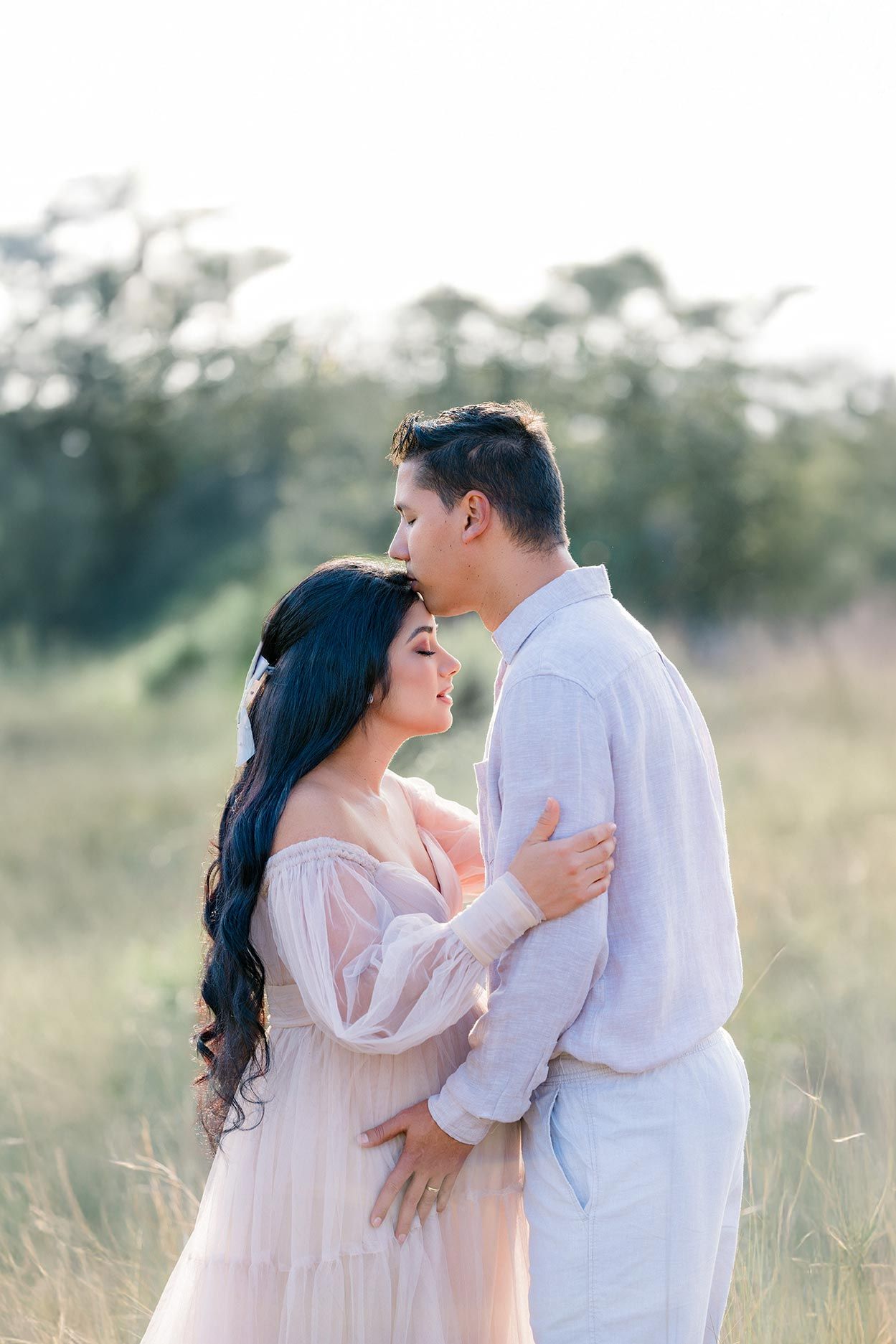 Romantic couple embraces in dreamy outdoor setting with soft lighting and tall grass at sunset.