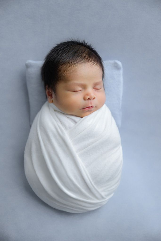 Sleeping newborn baby swaddled in white wrap on a soft blue background.