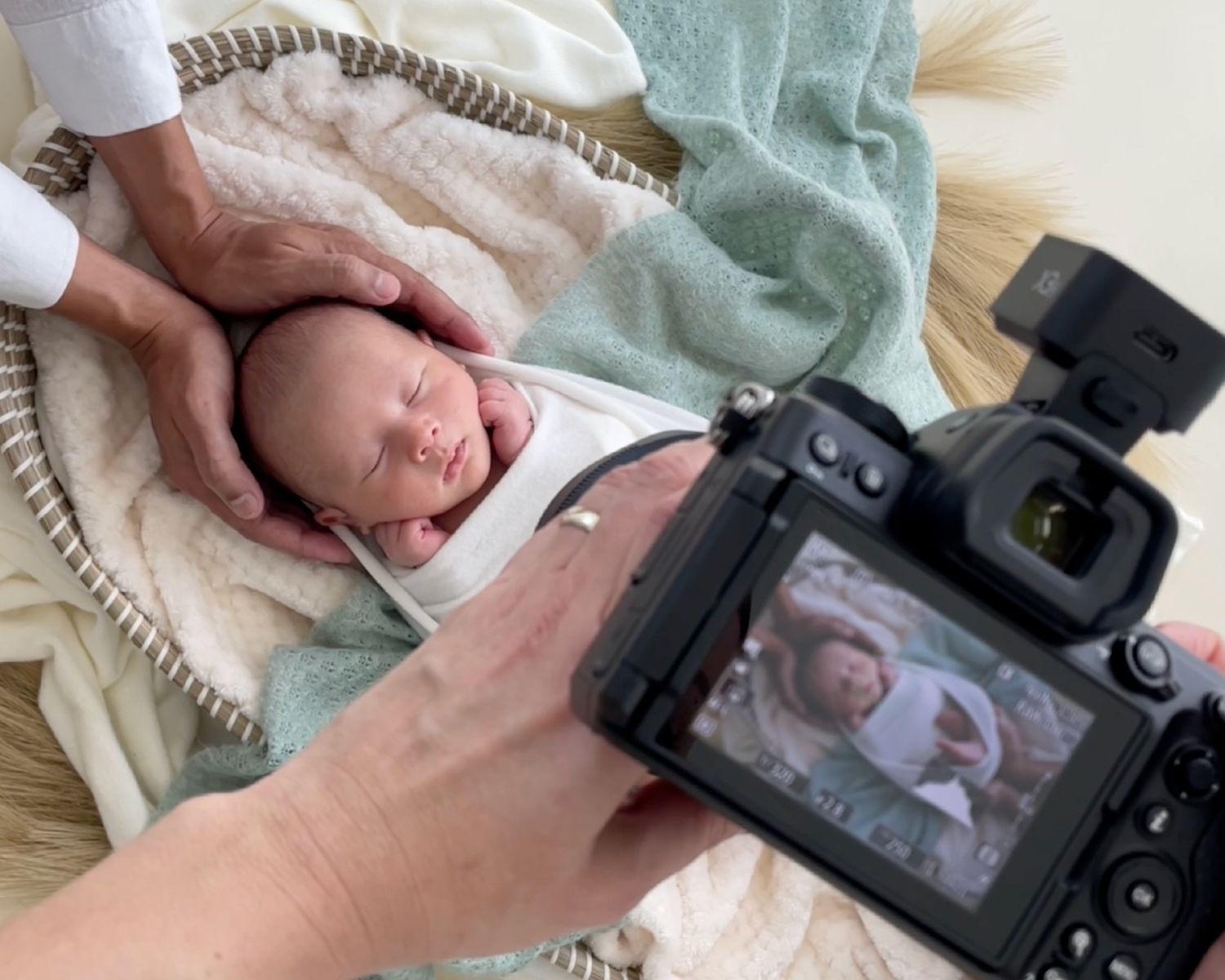 A digital camera captures a photo of a sleeping newborn baby wrapped in soft blankets during a photography session.
