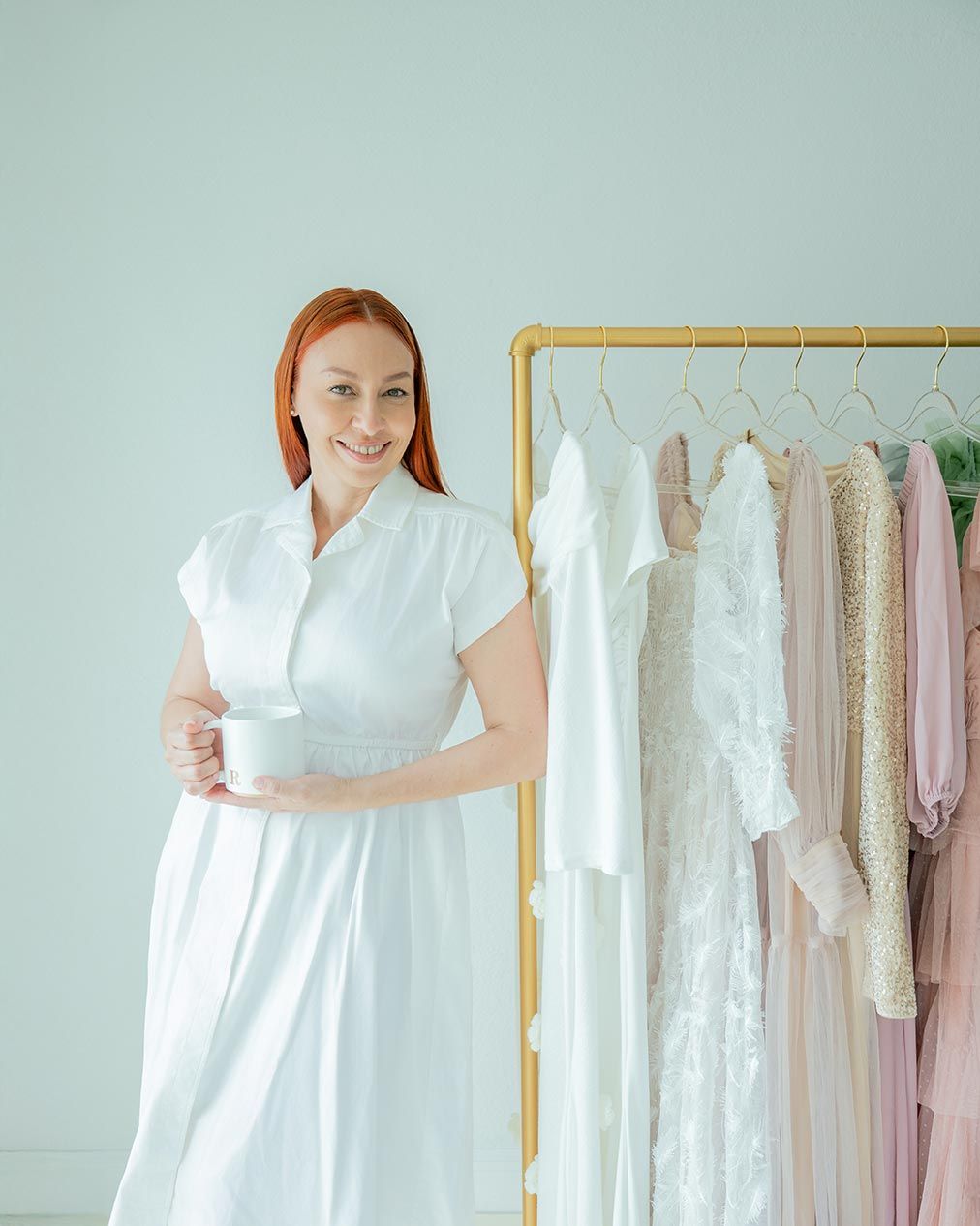 Fashion scene with clothing rack displaying pastel dresses and a figure in white dress standing next to it near mint green wall.