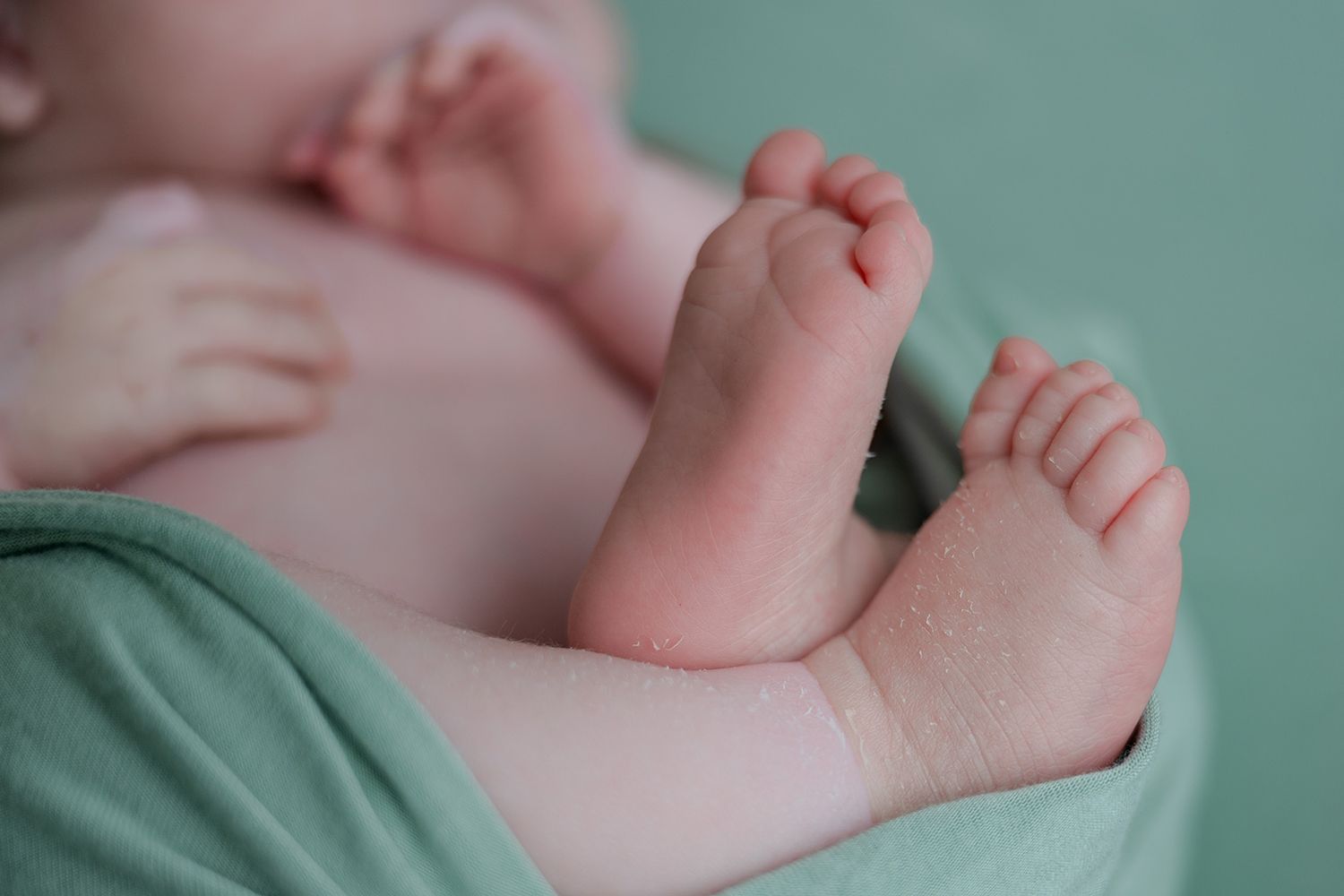 Close-up of newborn baby feet and tiny toes wrapped in a soft green blanket.