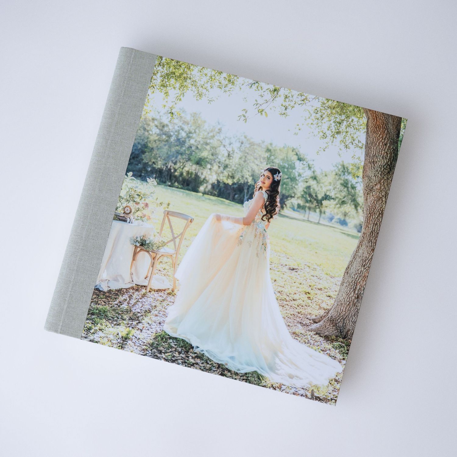 Elegant wedding photo album with linen cover featuring a bride in a white gown standing under a tree in a lush garden.