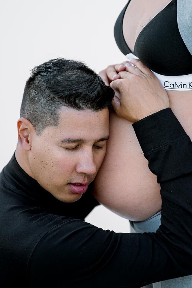 A loving maternity photo shows a person embracing a pregnant belly wearing a Calvin Klein bra.