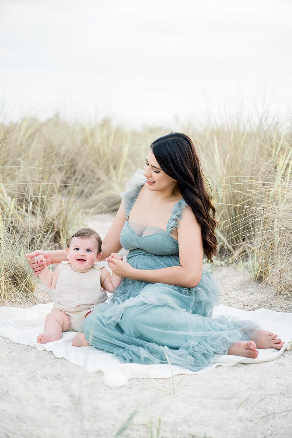 Sweet family portraits on white sand beach with mother in flowing turquoise dress and baby.