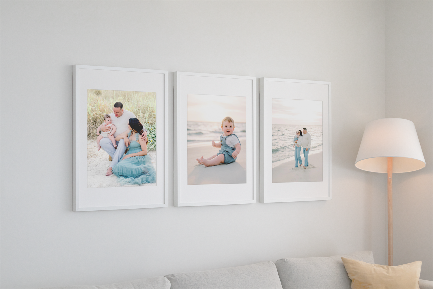 Three white-framed family photos hang on a gray wall above a couch, with a white table lamp visible to the right.