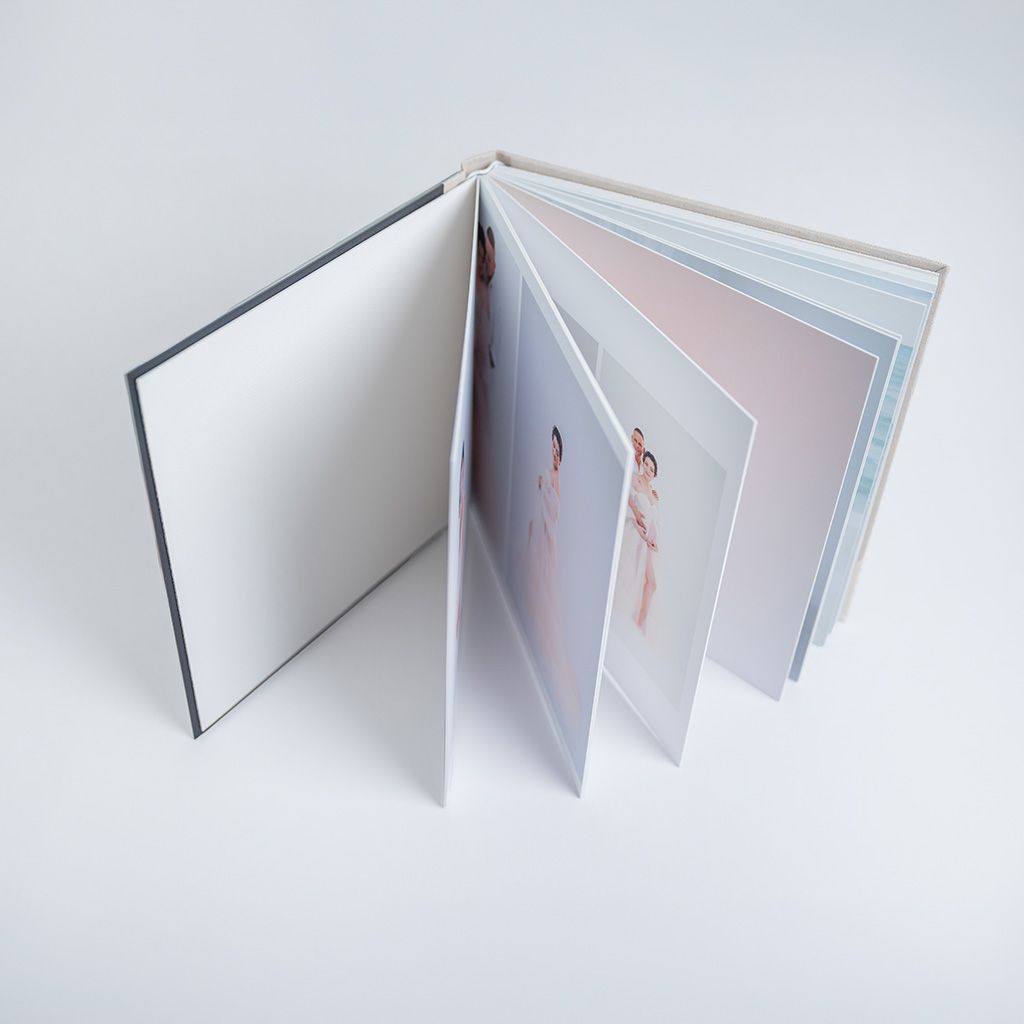 Open hardcover photo book displaying elegant fashion images in soft pink and blue tones on white background.