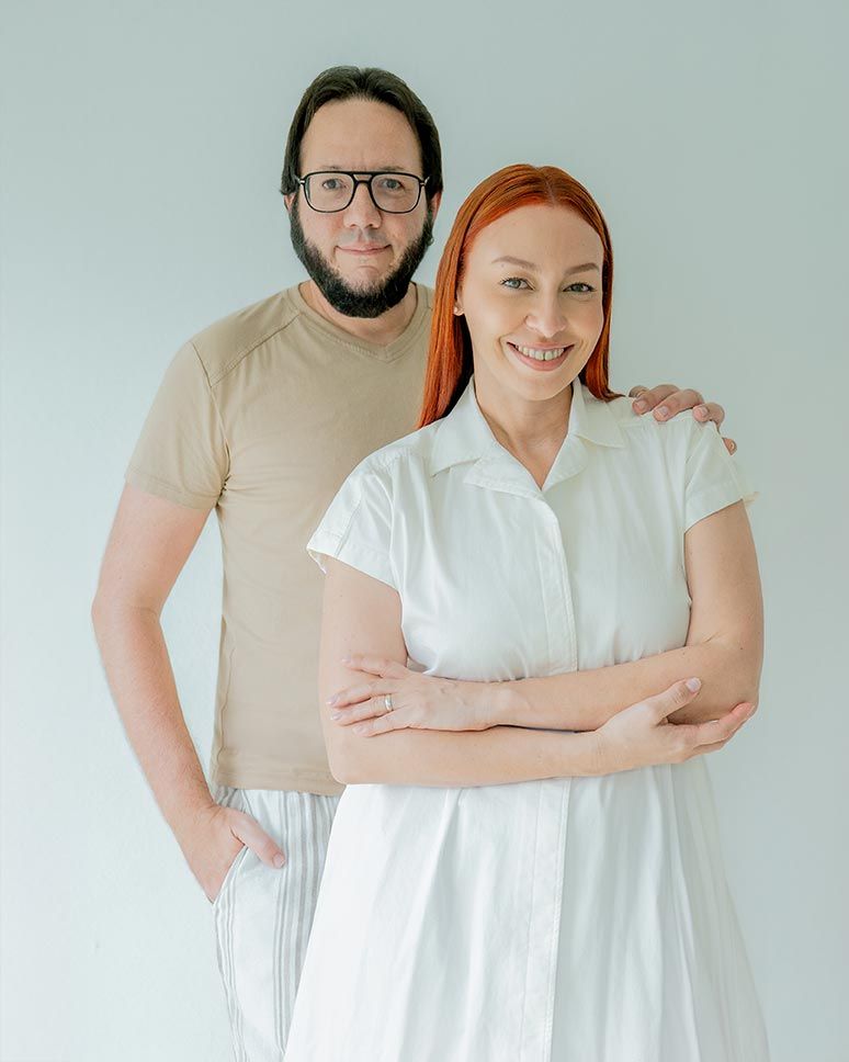Two adults in casual attire standing together against light background in studio portrait setting.