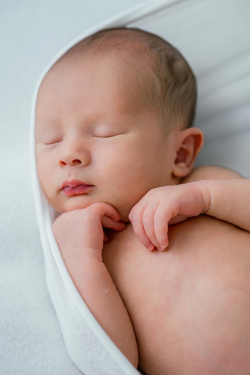 Peaceful newborn baby sleeping wrapped in a soft white blanket with tiny hands folded under chin.