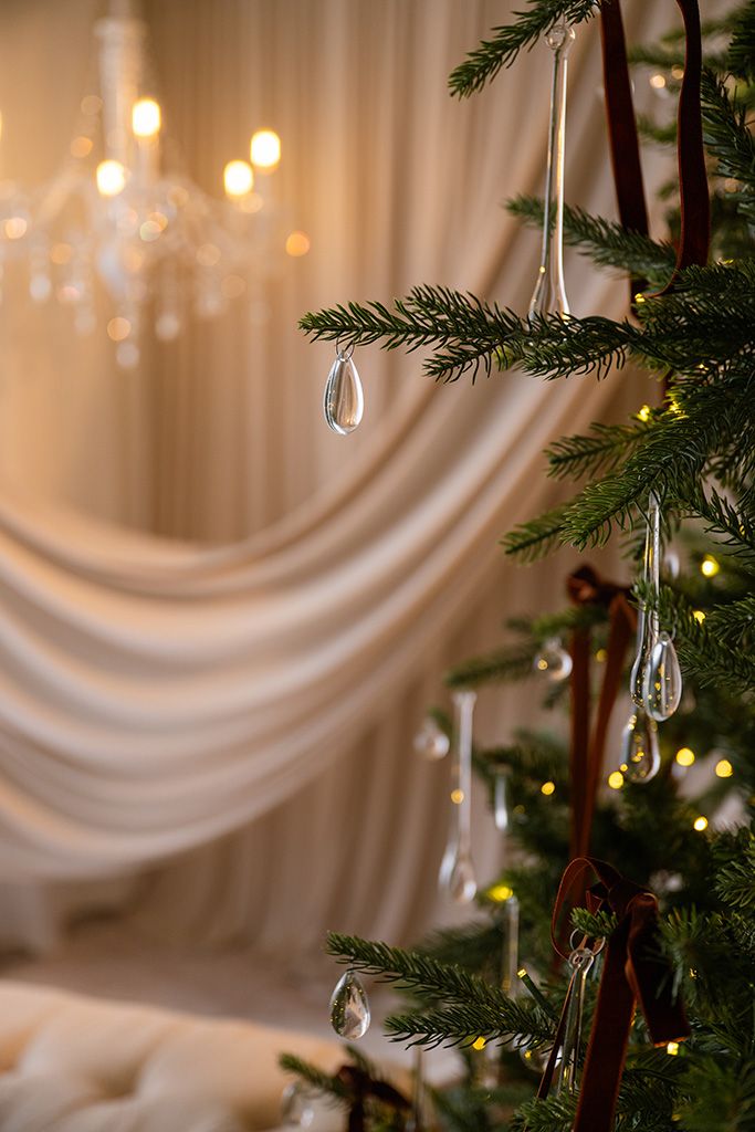 Christmas tree with crystal drop ornaments and red ribbons in an elegant room with warm glowing lights and white drapes.