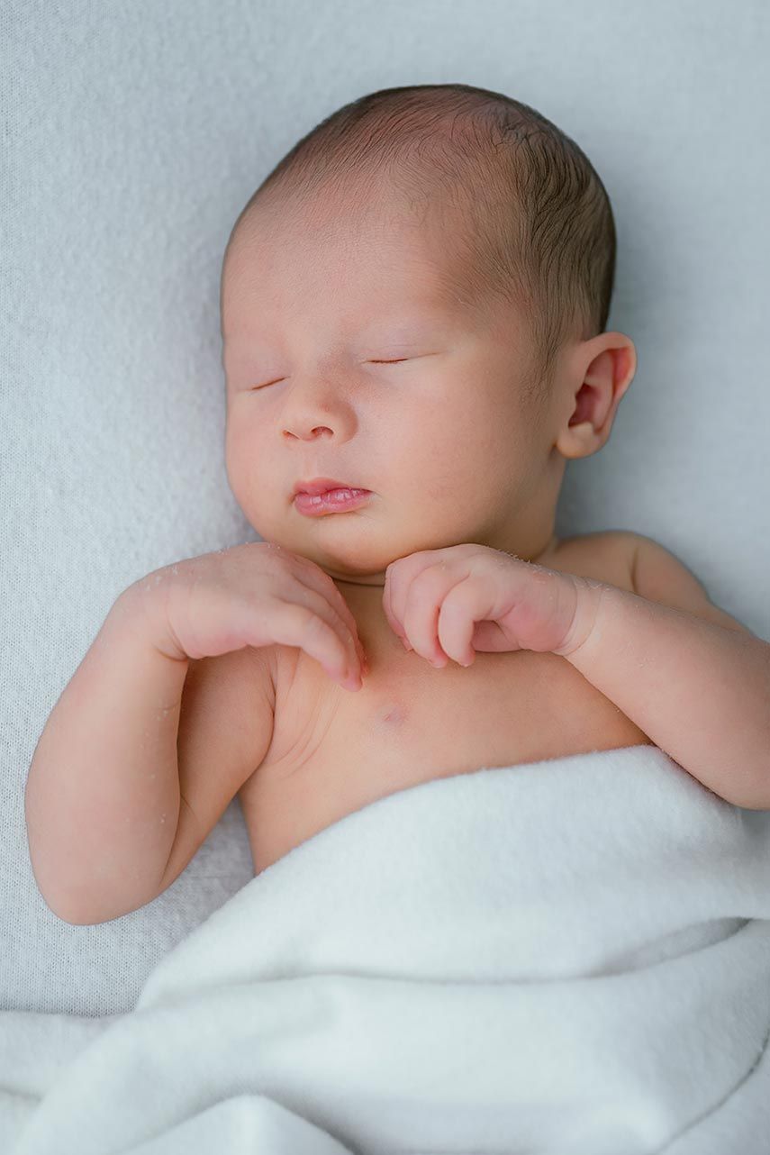 Peaceful newborn baby sleeping on a white blanket with eyes closed.
