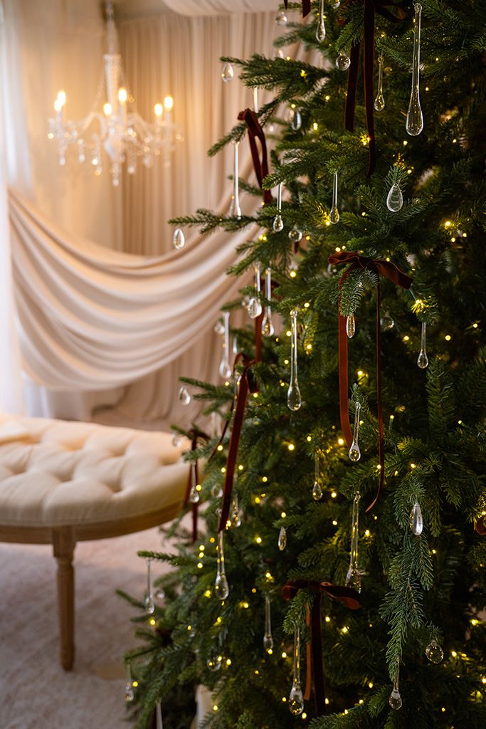 Elegant Christmas tree with crystal ornaments, burgundy ribbons, and warm lights in a luxurious white decorated room.