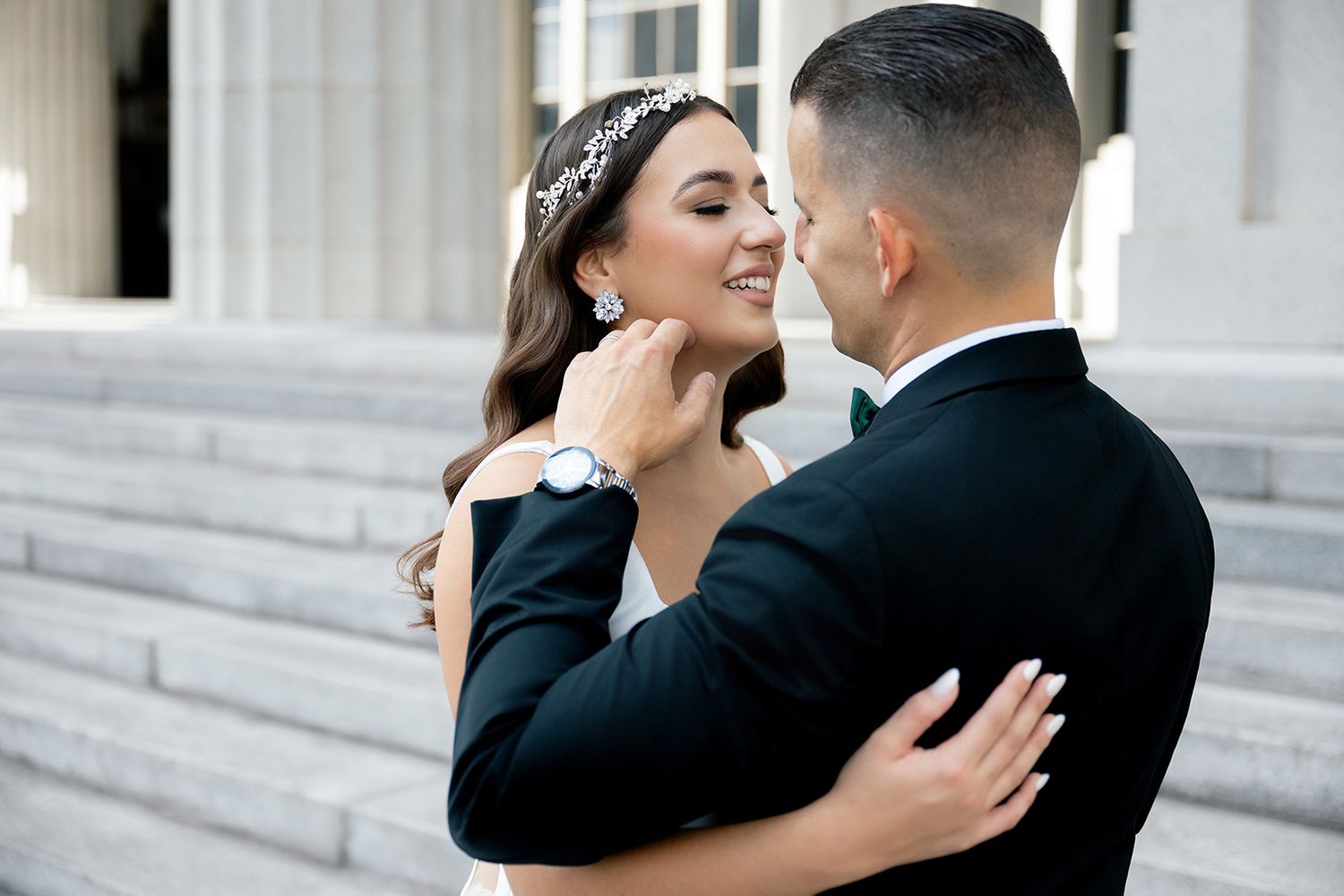 Bride and groom share a romantic embrace on wedding day, with bride wearing floral headpiece and elegant earrings.