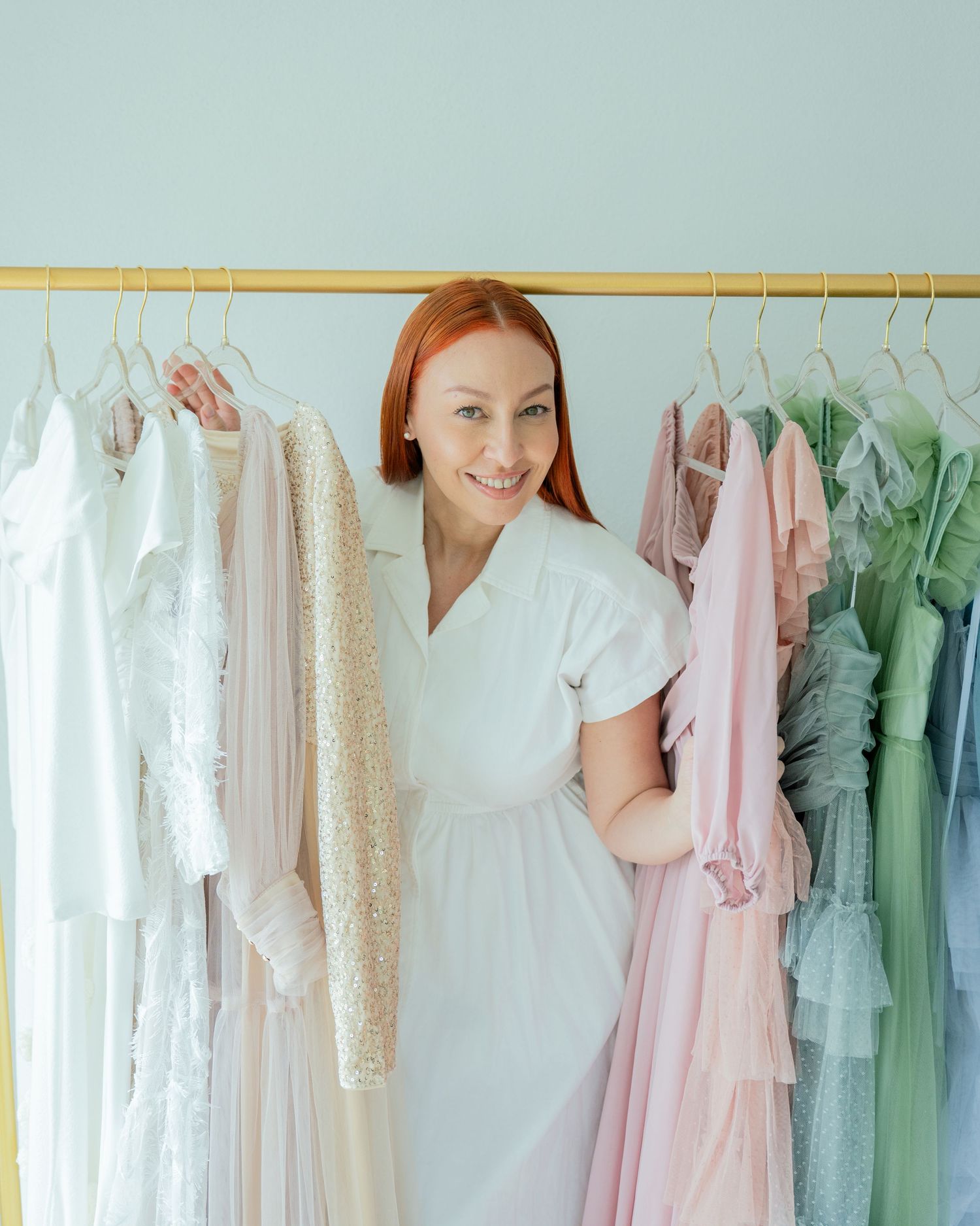 Elegant pastel formal dresses in pink, mint green, and white hang neatly on a clothing rack in a bridal boutique.