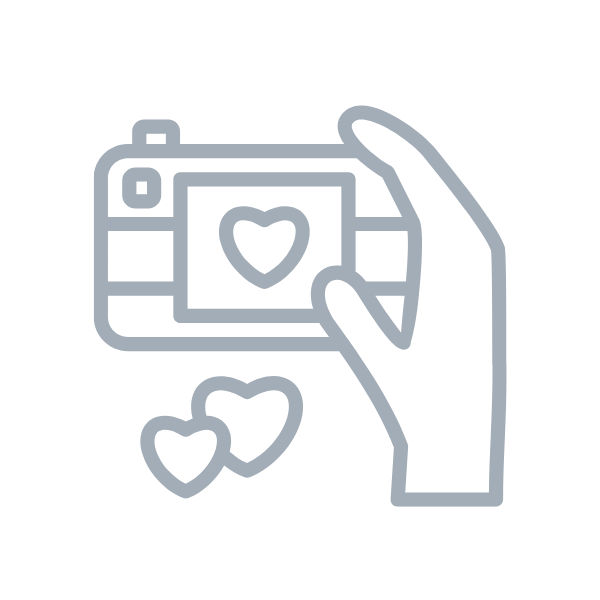 Simple line drawing of a hand holding a camera with a heart icon and two floating heart symbols below.