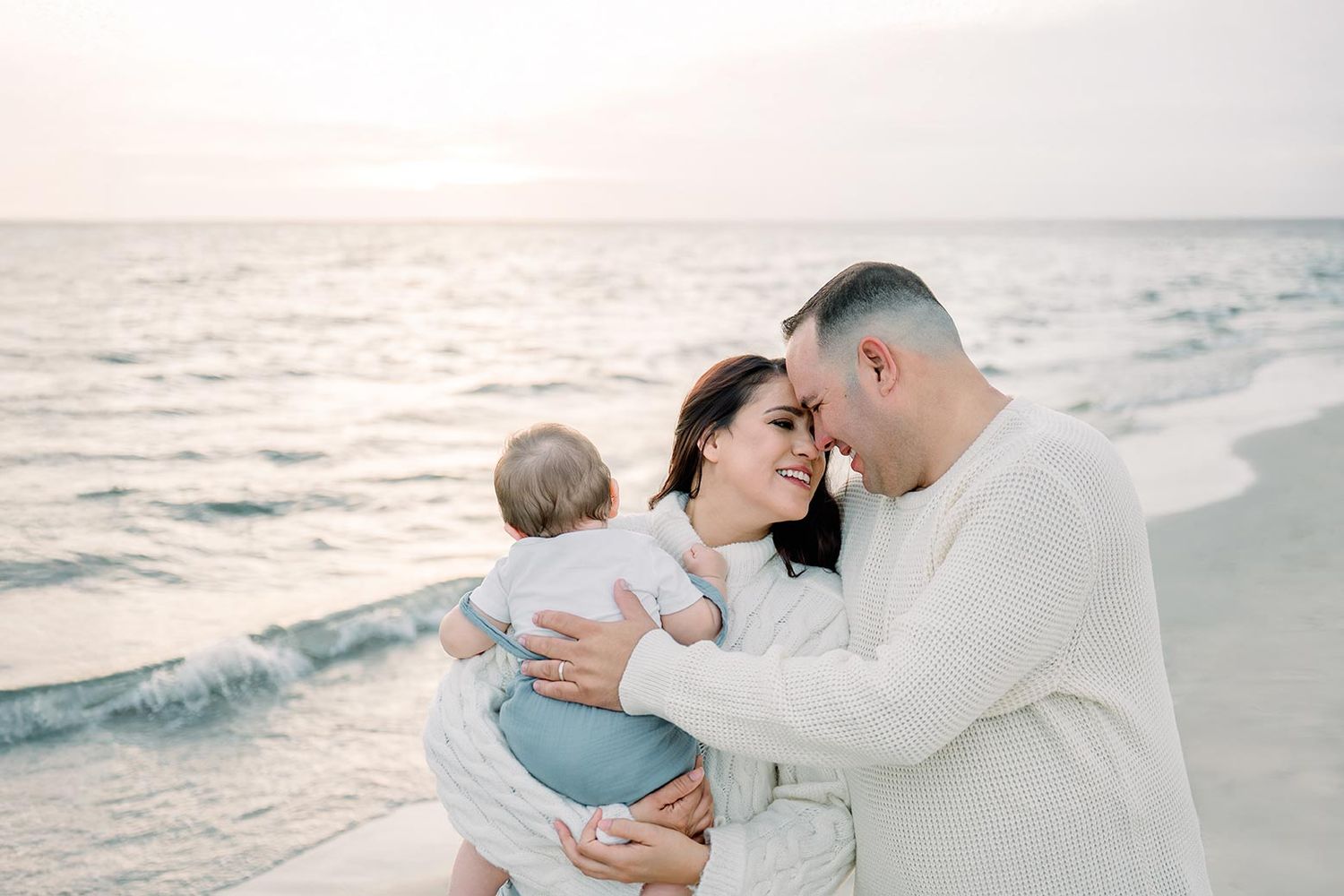 Sweet family moment captured against a soft pastel seascape backdrop during golden hour.