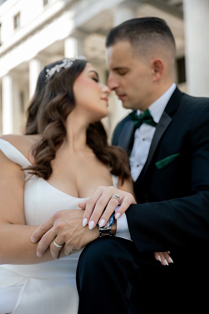 Close-up of bride and groom nearly kissing, hands intertwined showing wedding rings and watch.