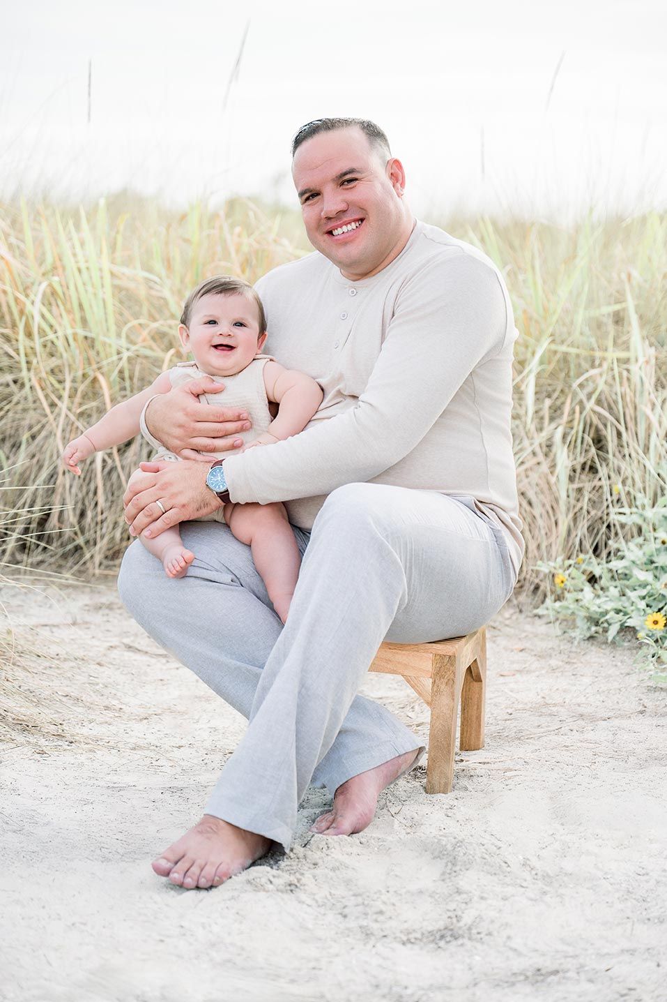 Family photographs at beach with light and airy setting show loving interactions on wooden bench in sand.