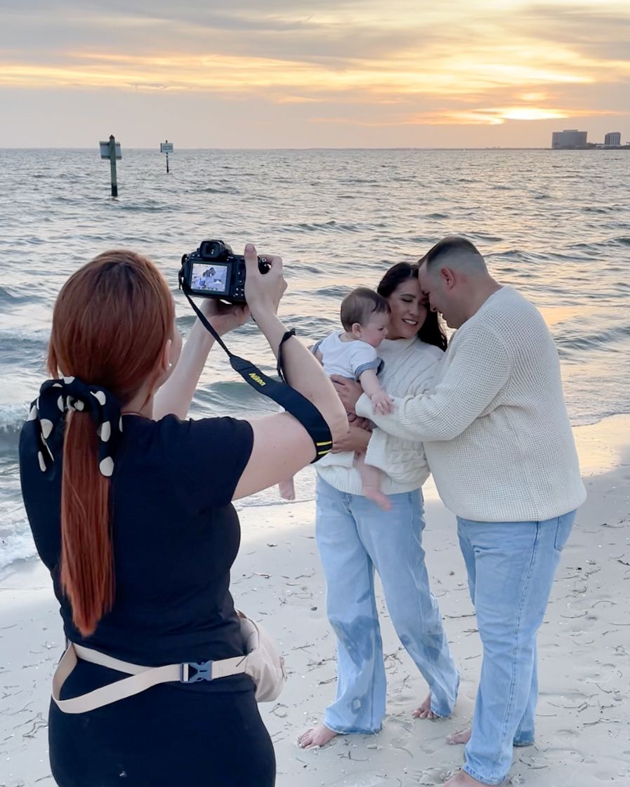 Professional photographer captures a photoshoot on the beach at sunset with subjects posing against the orange sky.