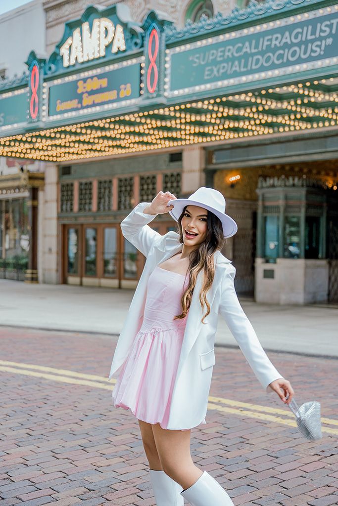 Stylish woman in pink dress and white blazer poses outside Tampa Theatre marquee advertising Mary Poppins.