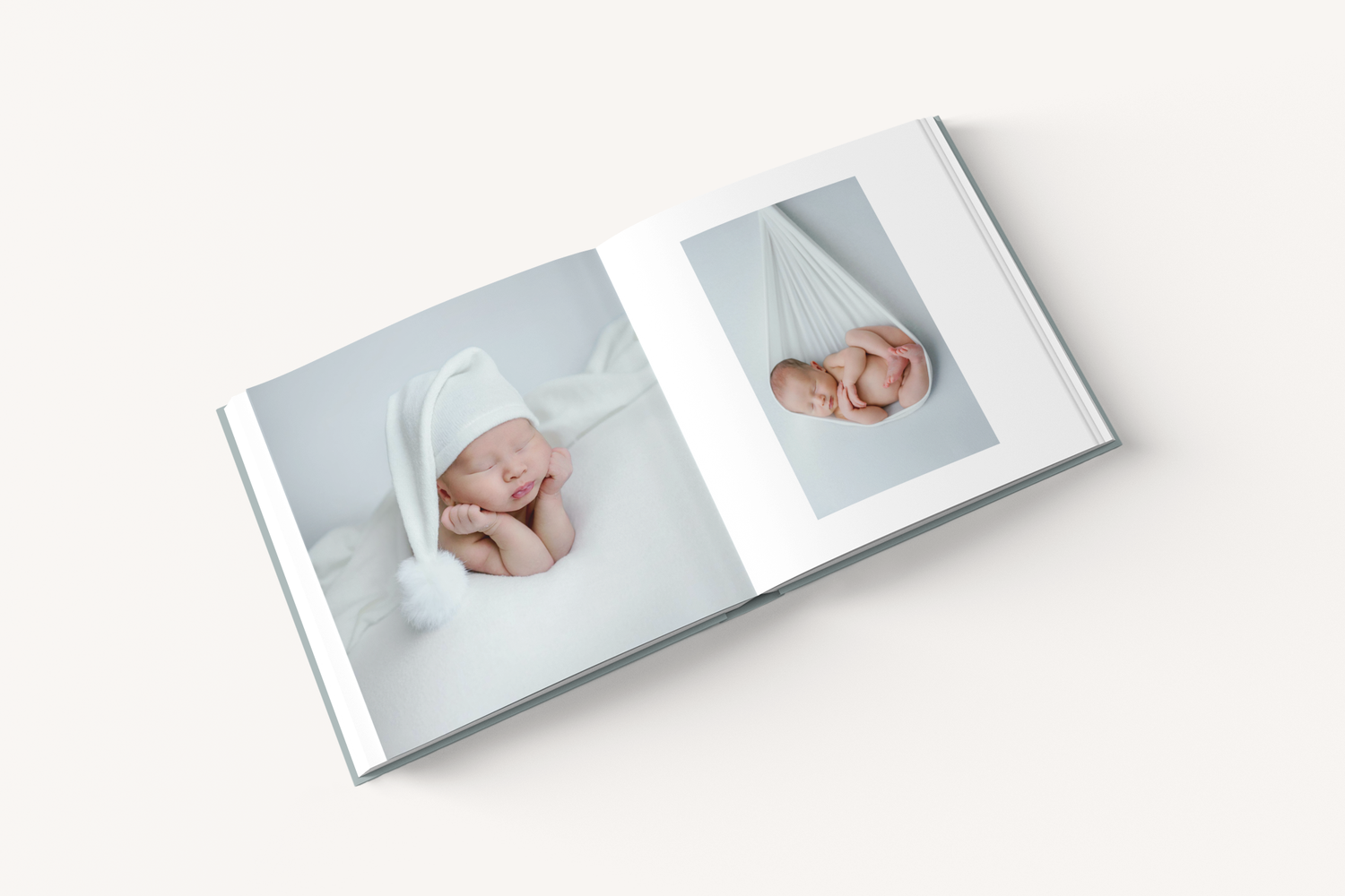 White photo album book opened to display two baby portraits with soft lighting against light background.