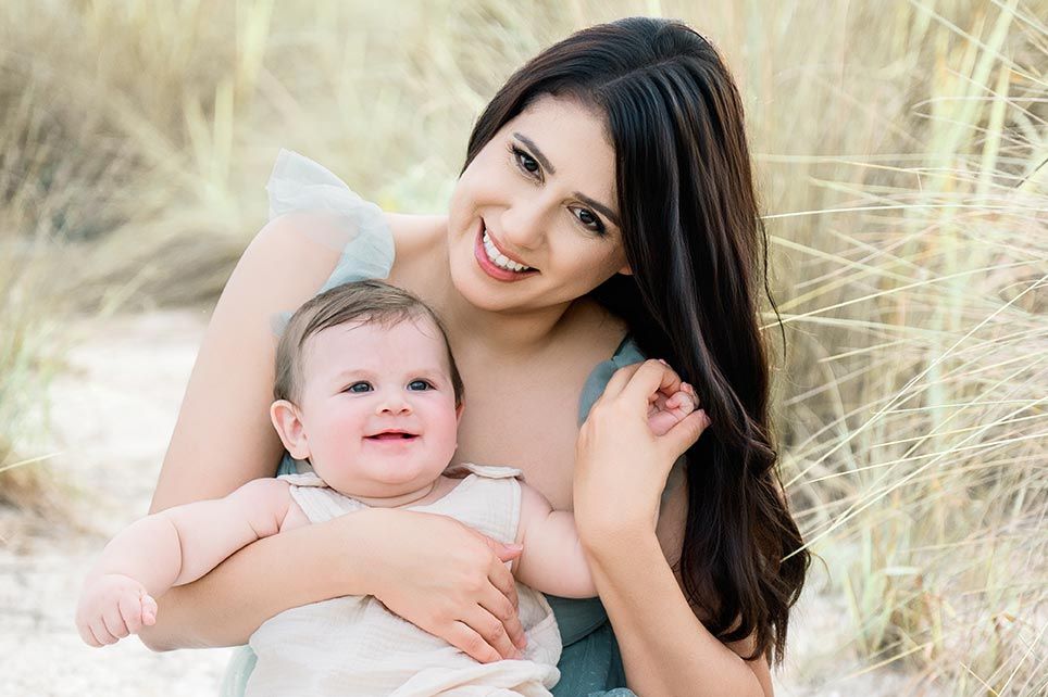 Candid beachside photoshoot of parent and infant playing together on sunny day.