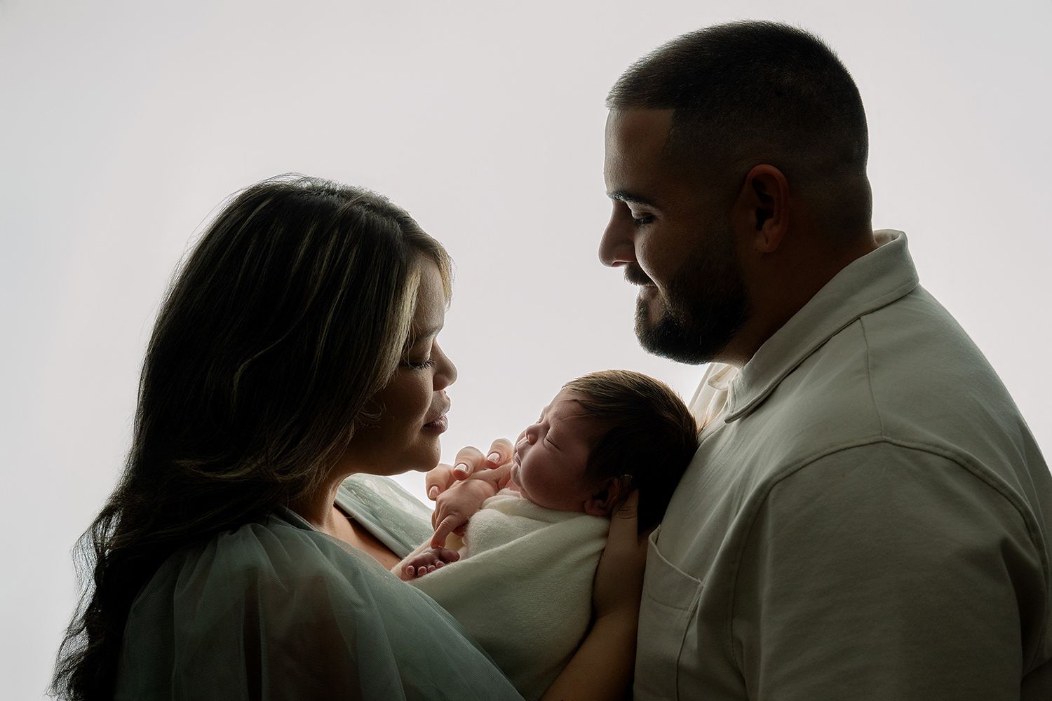 Parents gazing lovingly at their newborn baby in a soft, light-filled newborn photography session.