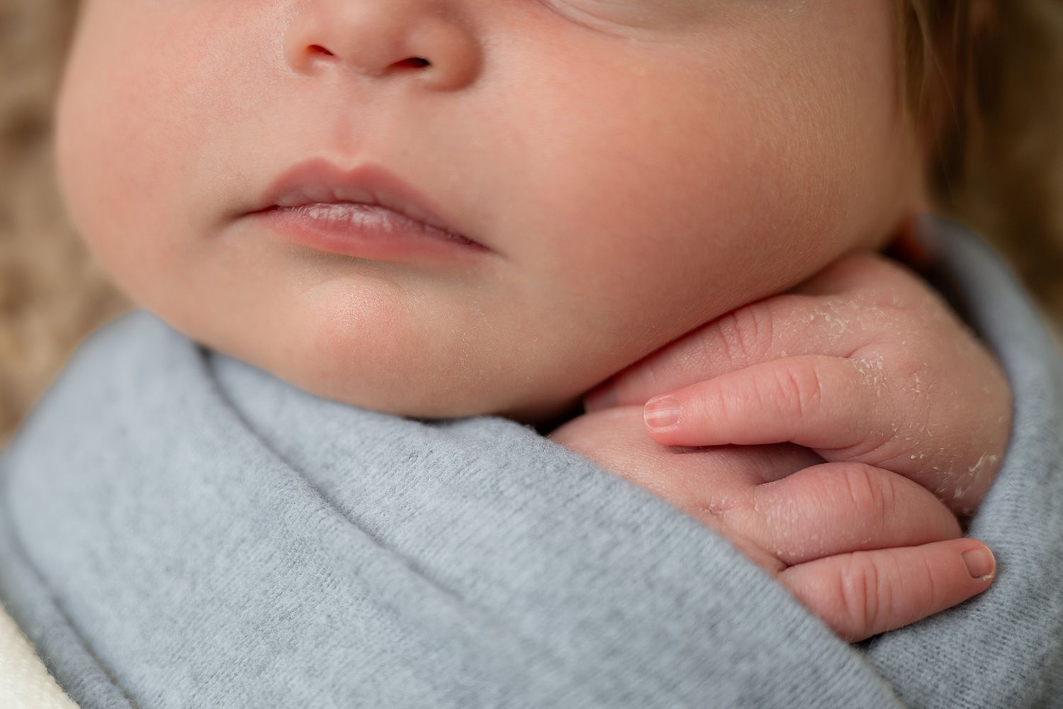 Close-up of a sleeping newborn baby wrapped in a soft blue swaddle blanket with tiny fingers visible.