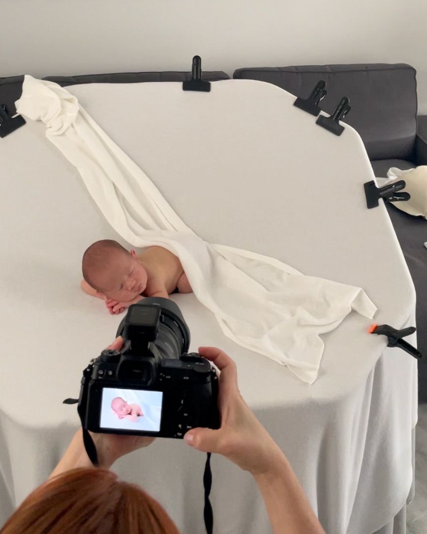 Behind-the-scenes newborn photography session showing camera LCD display and baby posed on white backdrop.