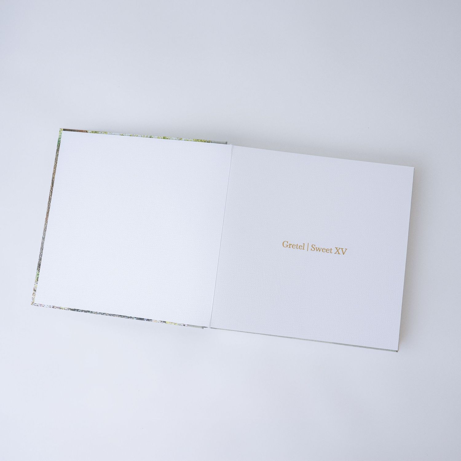 Open hardcover photo book with white pages and gold foil text reading 