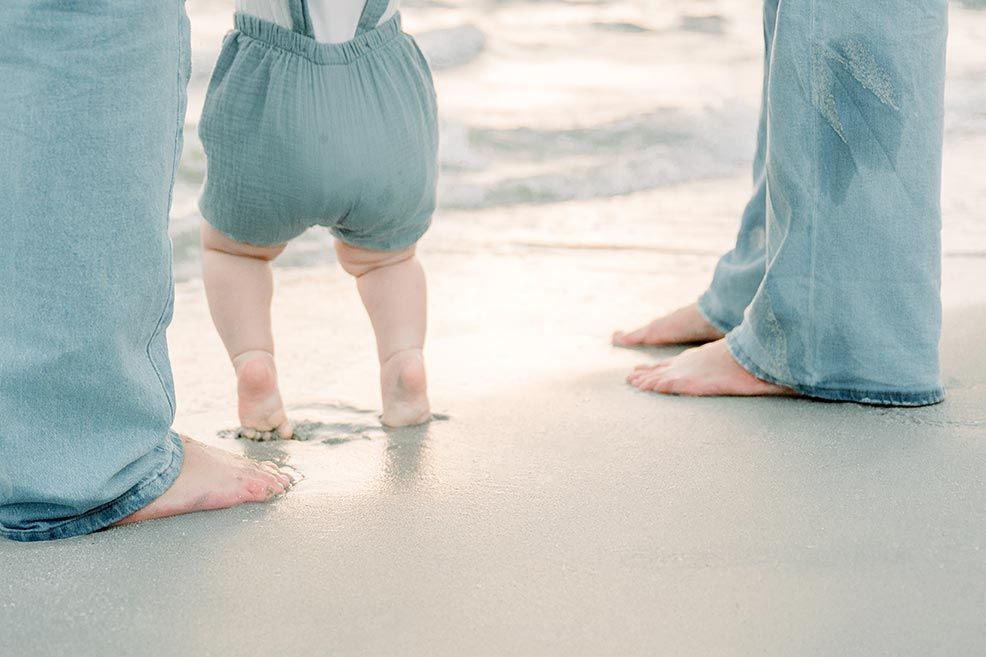 Bare feet of adults and child standing in wet sand at ocean's edge.