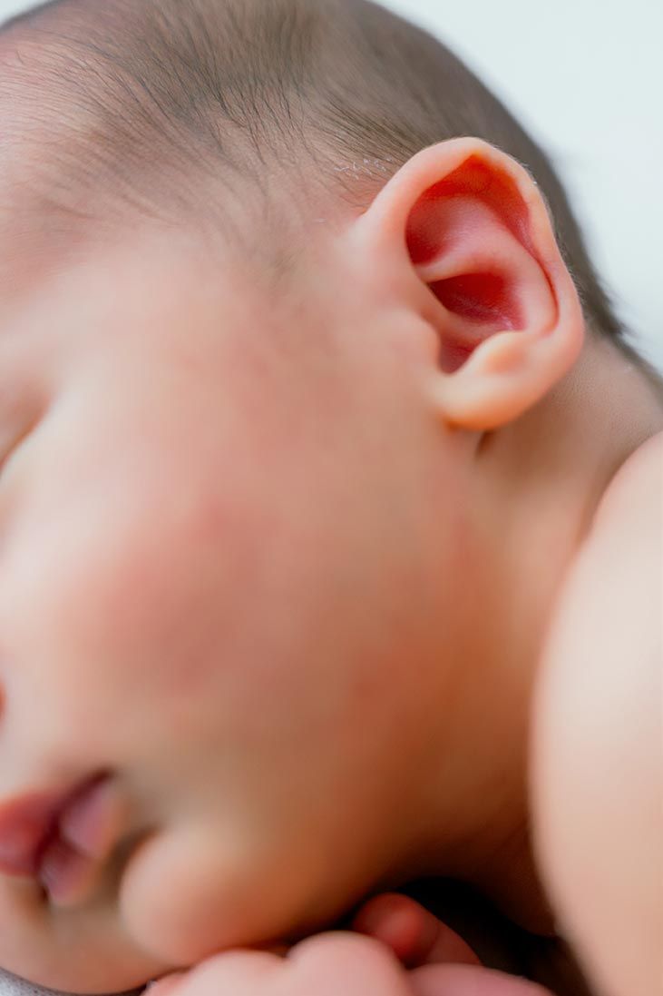 Close-up of a sleeping newborn baby's ear and profile, showing delicate skin and tiny features.