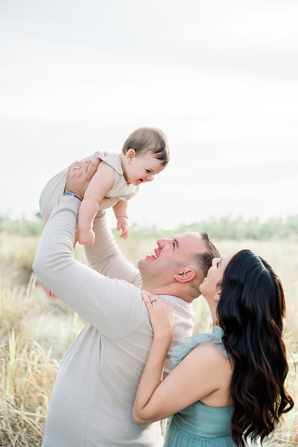 A loving family shares a joyful moment together in a sunlit field of tall grass.