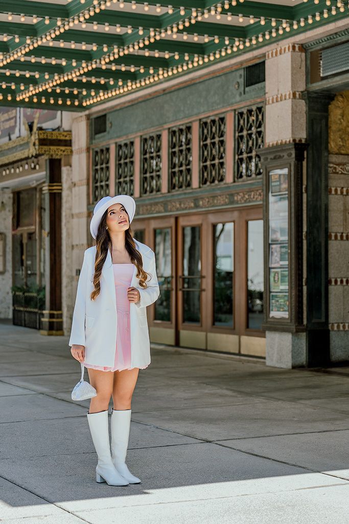 Young woman in pink dress, white blazer and bucket hat posing outside ornate Tampa Theatre entrance.