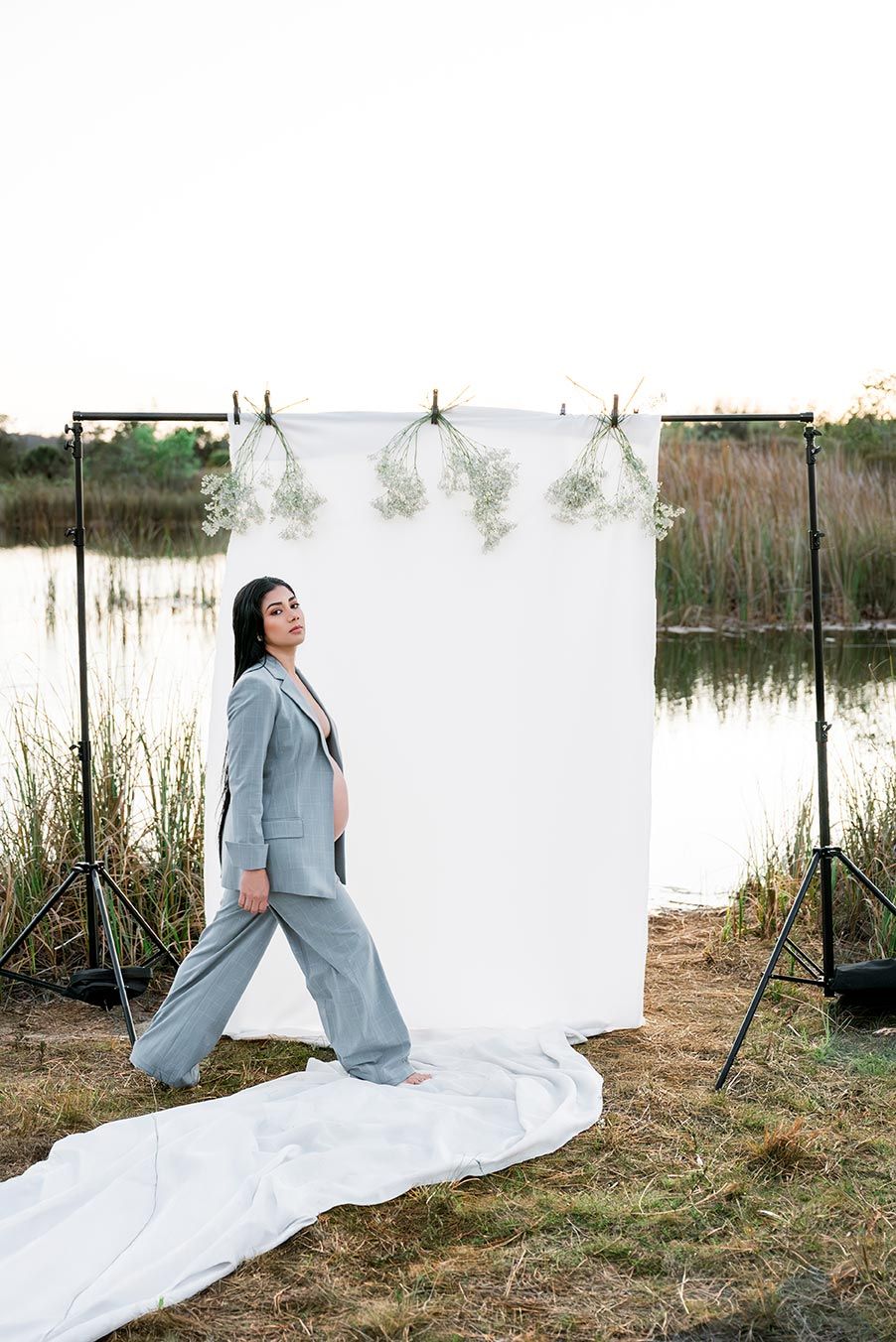 Behind-the-scenes view of outdoor photography setup with white backdrop and professional lighting in natural setting.
