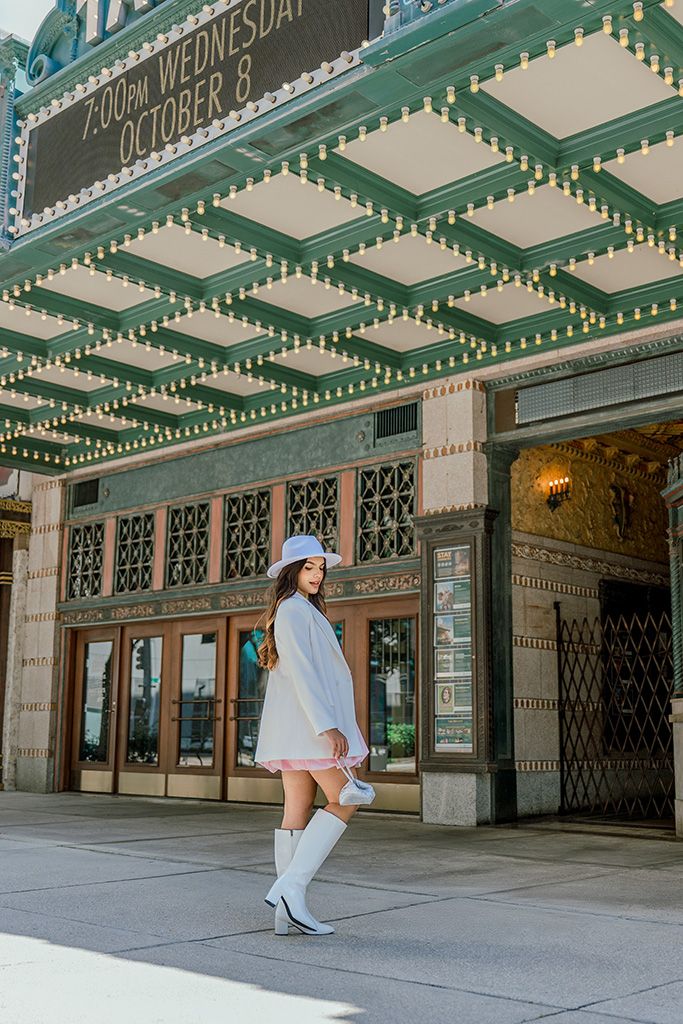 Fashionable woman in white outfit and hat poses sideways under Tampa Theater marquee on Wednesday.